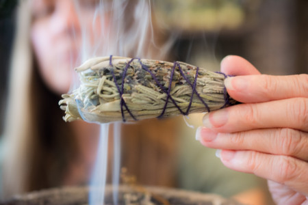 A woman holds a smoking bundle of sage and other herbs close to the camera