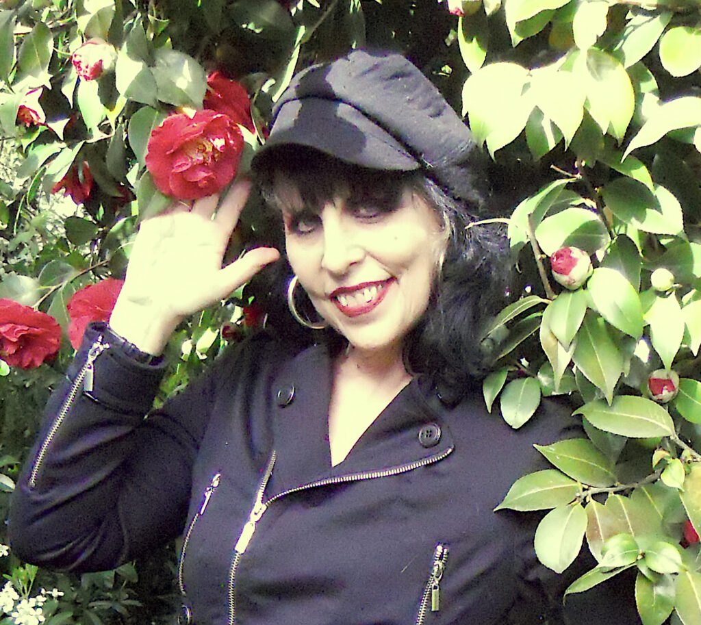 a woman in a black hat and black jacket holding a red flower