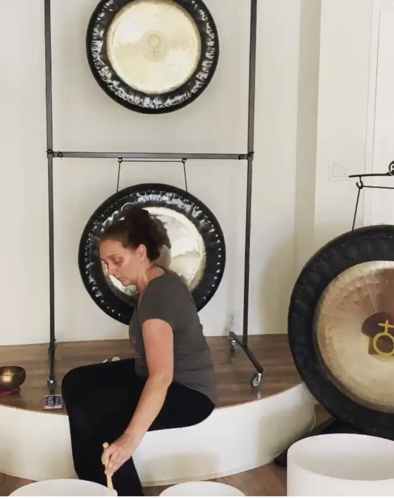 a woman sitting on a stage with gongs on the wall