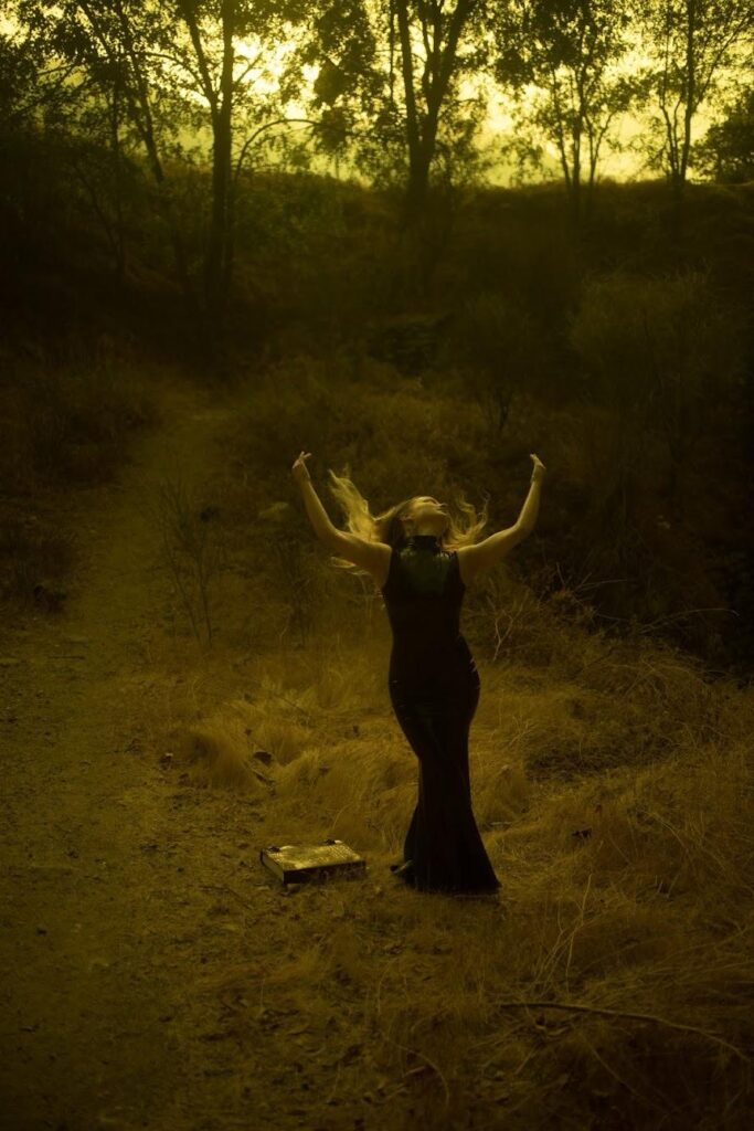 a woman in a black dress with her arms up in the air