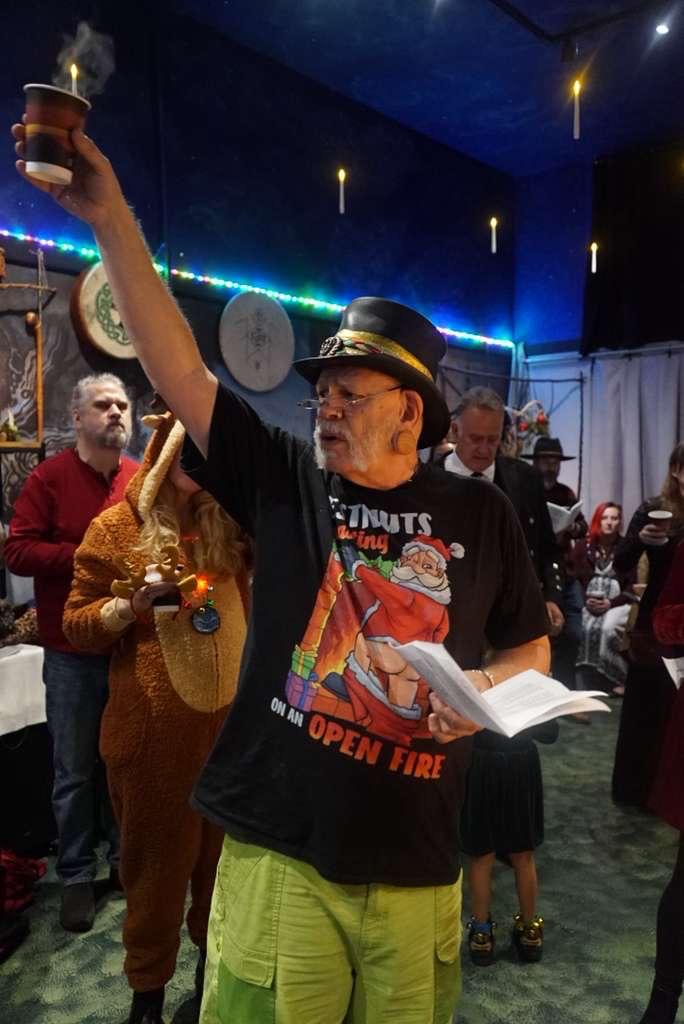 Griffin Ced holding a book of carols and leading a toast of wassail